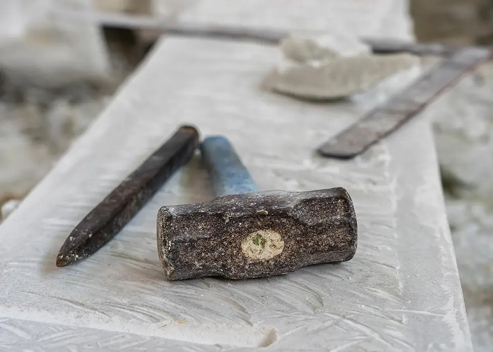 Bildhauerwerkzeuge auf einer Marmorplatte, Nahaufnahme. Arbeitsplatz, traditioneller Werkzeugen Bildhauer, rote Kreide, Lineal, Hammer und Kapelle für die Bearbeitung von Stein.