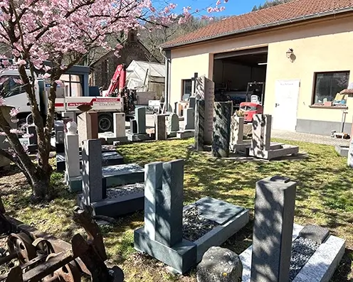 Firmengelände Schwenk In der Hofeinfahrt von Steinmetz Schwenk steht der eigene LKW und viele Steinarbeiten und einem Kirschbaum