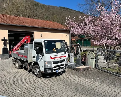 Firmengelände Schwenk In der Hofeinfahrt von Steinmetz Schwenk steht der eigene LKW und viele Steinarbeiten und einem Kirschbaum